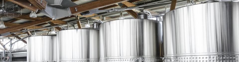 A row of large stainless steel process vessels beneath an industrial roof structure.